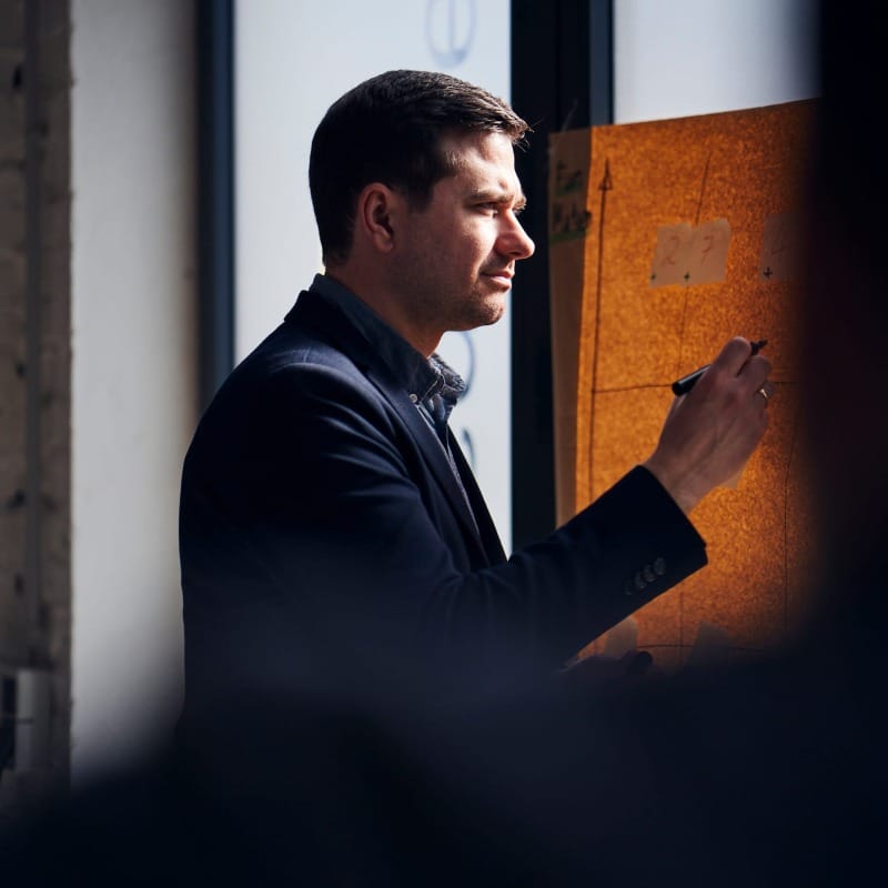 Markus Mazur schreibt konzentriert an einem Flipchart, Seitenansicht, natürliches Licht, Büroumgebung.